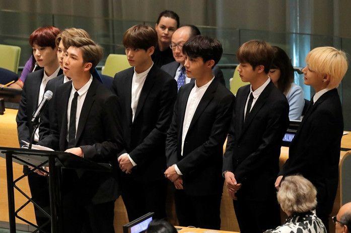 Korean idol group members giving a speech at the United Nations, symbolizing global influence of K-pop.