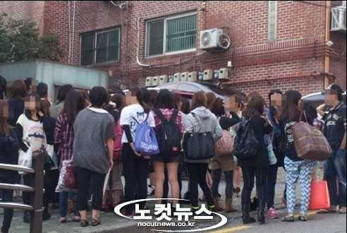 Large group of fans waiting outside a building for K-pop idols, highlighting the vibrant fan club culture in Korea.