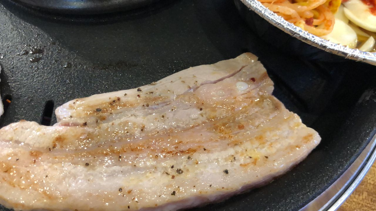 一盘在烤架上烤制的韩式五花肉片，表面略带金黄色泽，展现出丰富的油脂感。