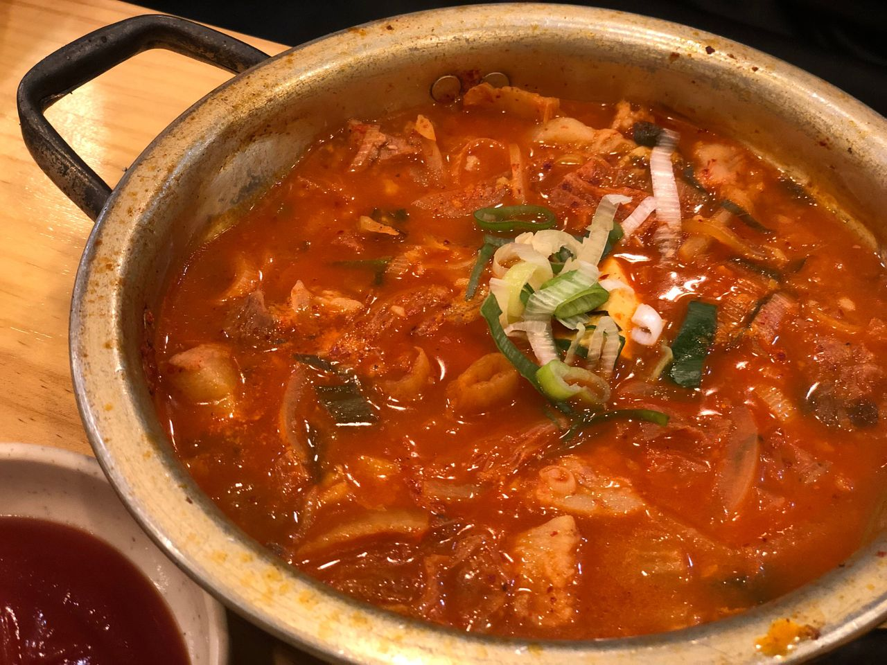 一碗热气腾腾的泡菜锅，内含丰富的蔬菜和肉块，呈现出浓郁的红色汤底。