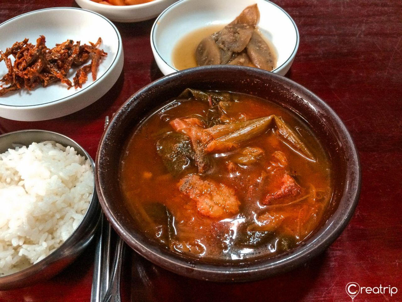 一碗红色汤底的辣牛肉汤，上面撒有葱花，锅中能看到肉块和线状萝卜丝。