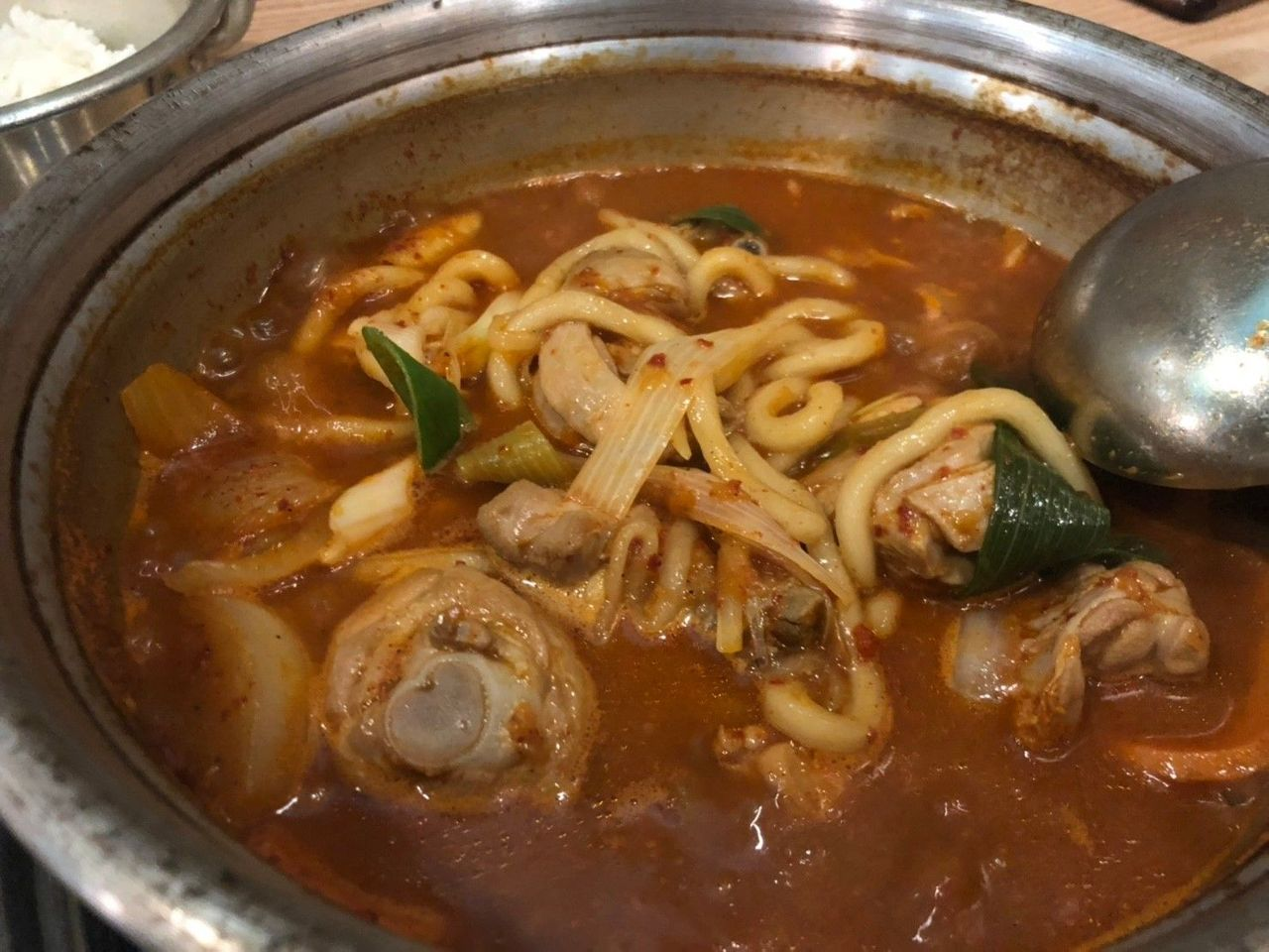 安东辣炖鸡，红色汤汁里包含着浓郁的鸡肉、洋葱、土豆，面条点缀其中。