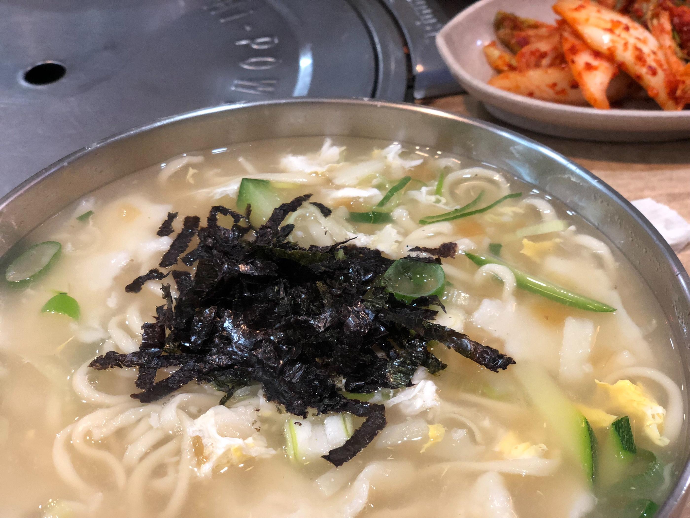 传统韩式刀削面，配有韩国泡菜作为佐料，置于金属碗中，令人垂涎。