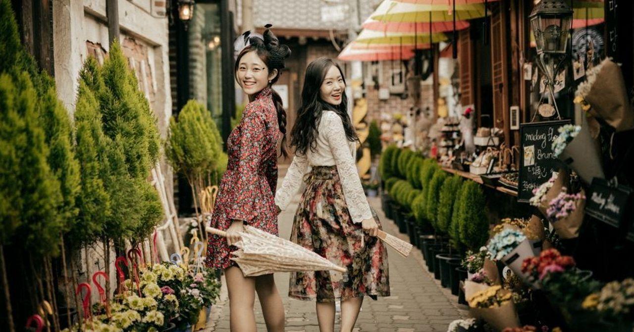 益善洞街巷中，兩位女性身穿復古古典服裝，撐傘漫步在充滿花草和傳統韓屋的街道上，享受休閒時光。