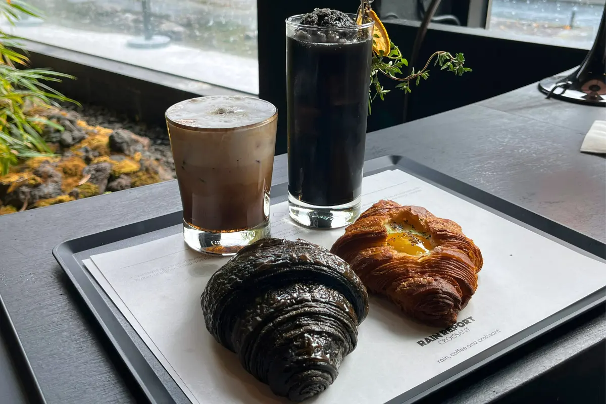 RAIN REPORT Croissantのトレイに乗せられたクロワッサンとドリンク。黒いクロワッサンとイエローカスタードの入ったクロワッサンが見える。