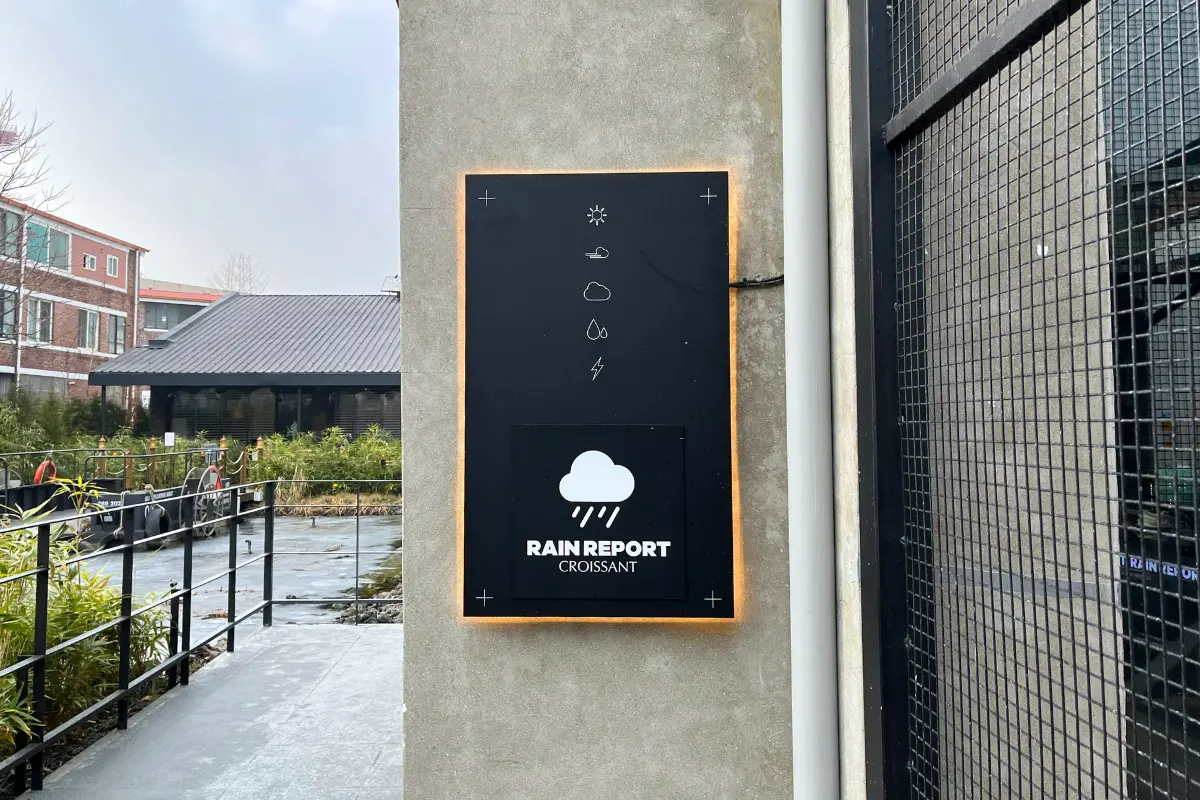 韓国のカフェRAIN REPORT Croissantの黒い看板と背景。看板には雨のシンボルが描かれている。