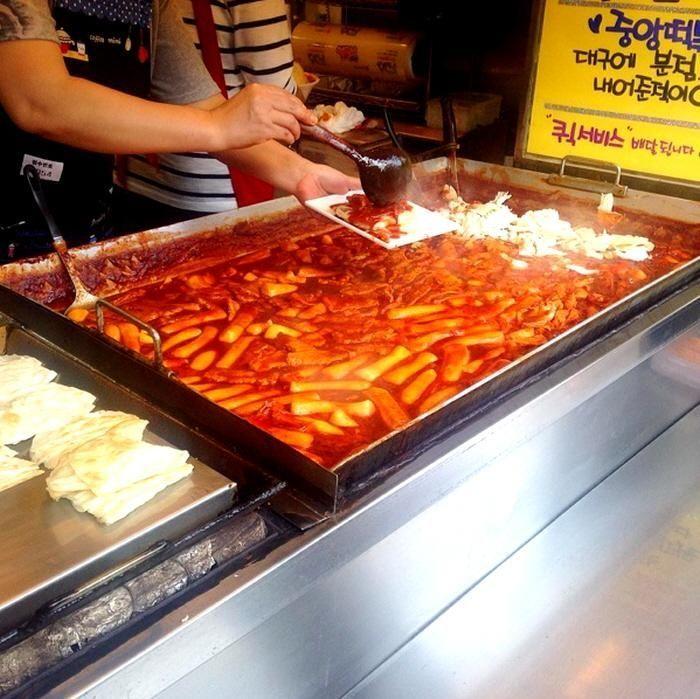 Preparing tteokbokki, a popular Korean street food, at a busy market.