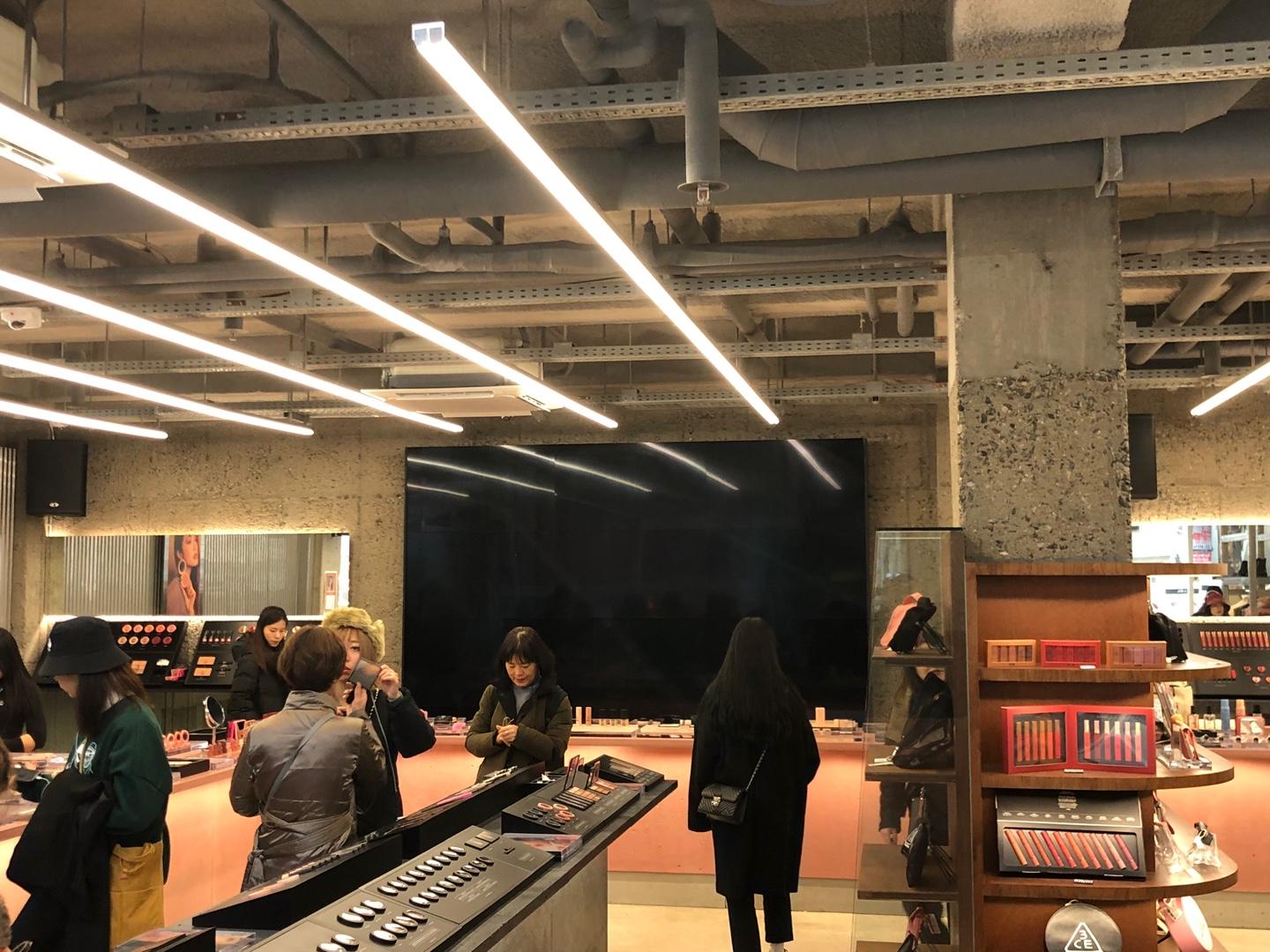 Intérieur du magasin STYLENANDA à Hongdae, mettant en vedette les produits cosmétiques 3CE sur les étagères, fort éclairage moderne.