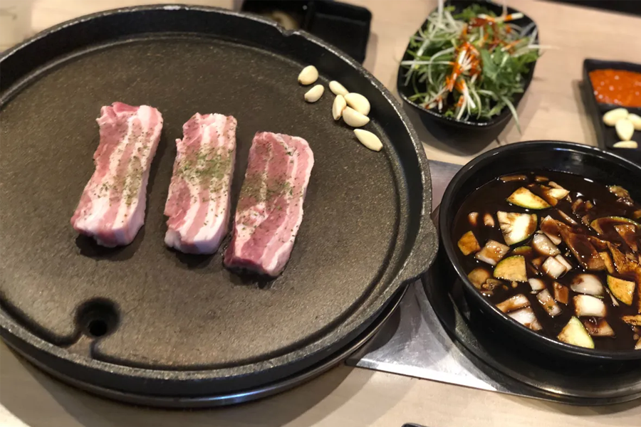 韓國豬肉大學的燒肉桌面，有豐富的燒肉、泡菜、蒜頭等食材供利用餐者選擇。