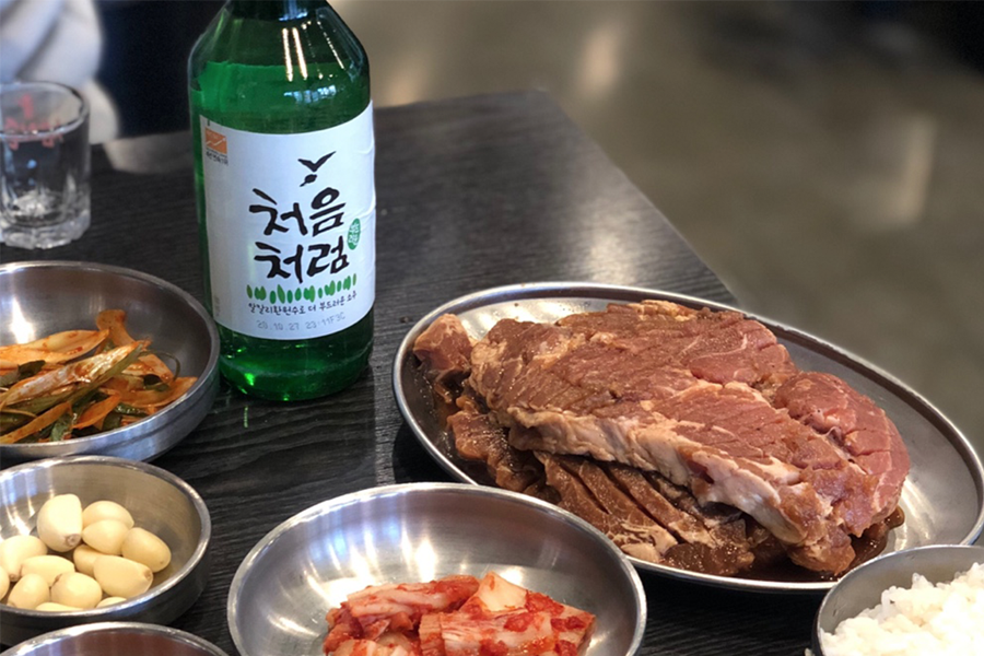 韓國弘大巨大排骨店的桌上，上面有燒肉、韓國燒酒和多樣配菜，準備美味的韓式燒肉餐。