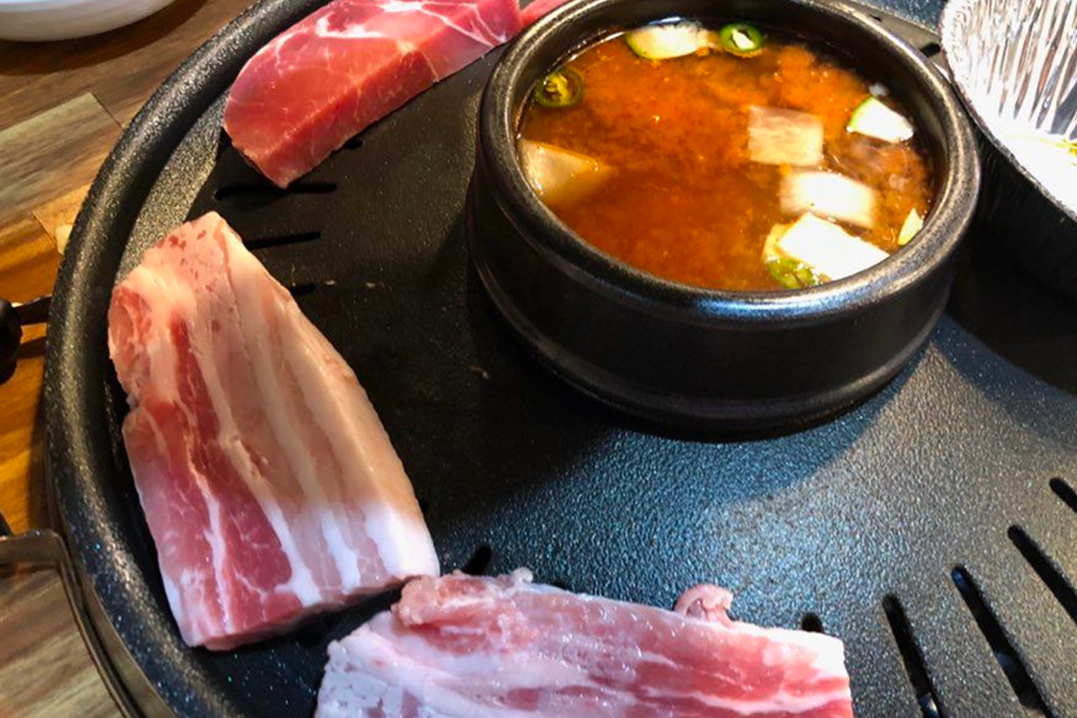 弘大荒謬的生肉店內的煎烤板，上面煎著豬三層肉搭配大醬湯，簡單方便的韓式烤肉吃法