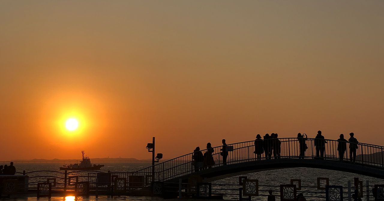 Tourist attraction recommendation in Incheon, South Korea, showcasing a sunset view over a bridge filled with silhouetted people.