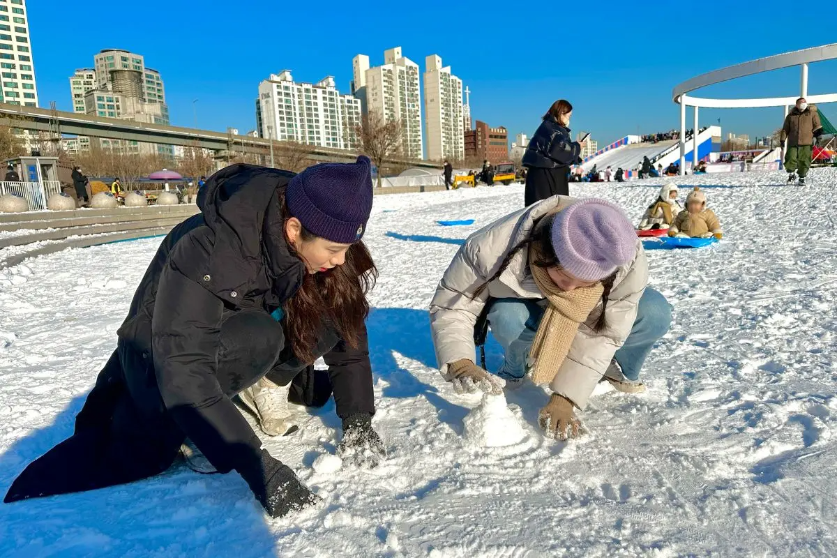 トゥクソム漢江公園の雪に覆われた広場で雪だるまを作る人々。冬のアウトドアアクティビティを楽しむ姿が見受けられます。