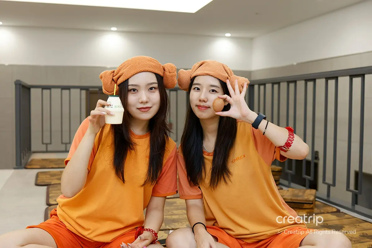 兩人在韓國汗蒸幕享受飲品，身著傳統蒸幕服裝，體驗悠閒時光。