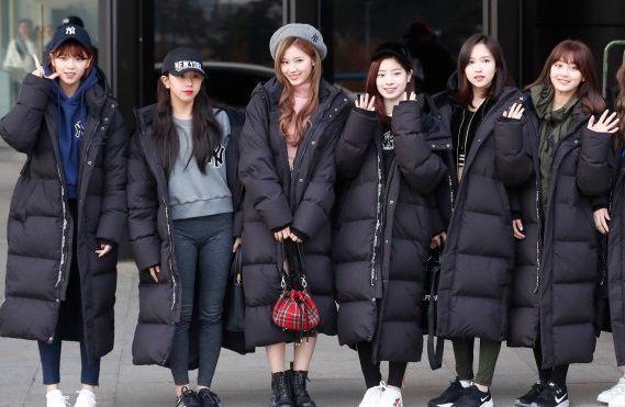 一群女子穿著厚重的冬季大衣，站在建築前，雙手插在口袋或揮手致意。