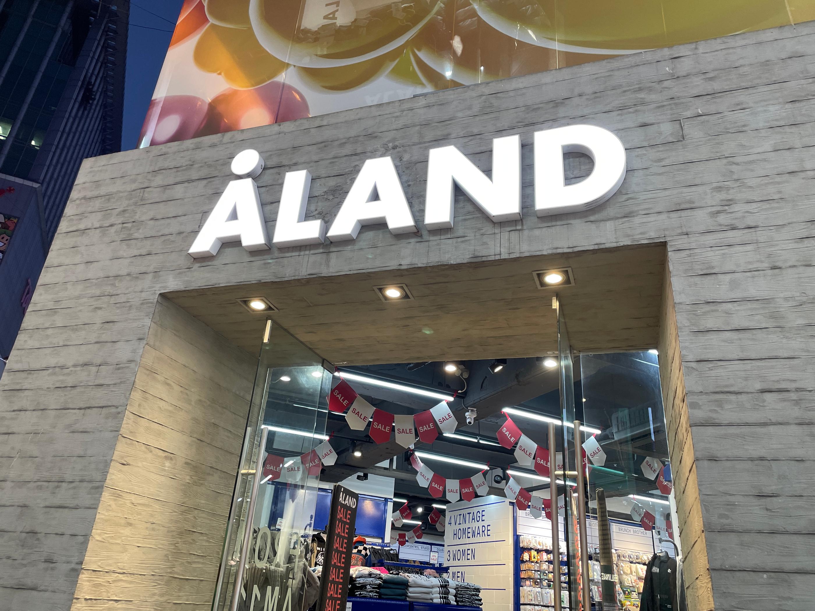 現代的な入り口が特徴のファッションストア、ALANDの外観。訪れた人々をセールのポスターが貼られたガラスドアが迎えます。