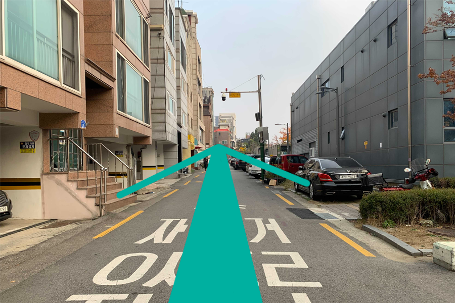 在韩国首尔的街景，一条安静的小巷，绿线箭头指示进入Lovin'Her咖啡厅的方向，体现了舒适的社区氛围。