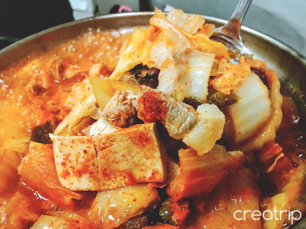 充滿韓式風味的泡菜鍋，內有豐富配料如豆腐、豬肉與泡菜，湯汁鮮紅濃鬱，展現地道韓國家常口味。