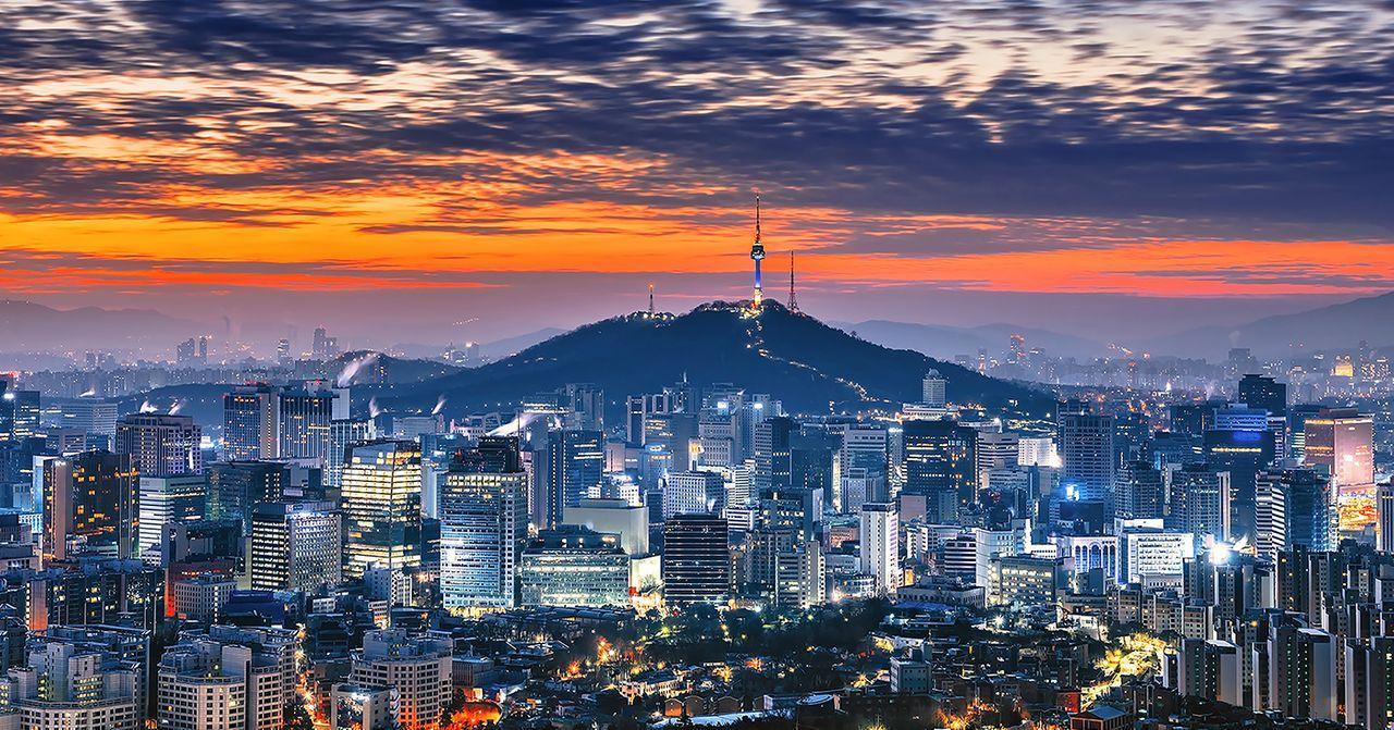 夕陽下的首爾夜景，遠處是N首爾塔，城市燈光灑在大樓之間，塑造出別樣的浪漫都市氛圍。