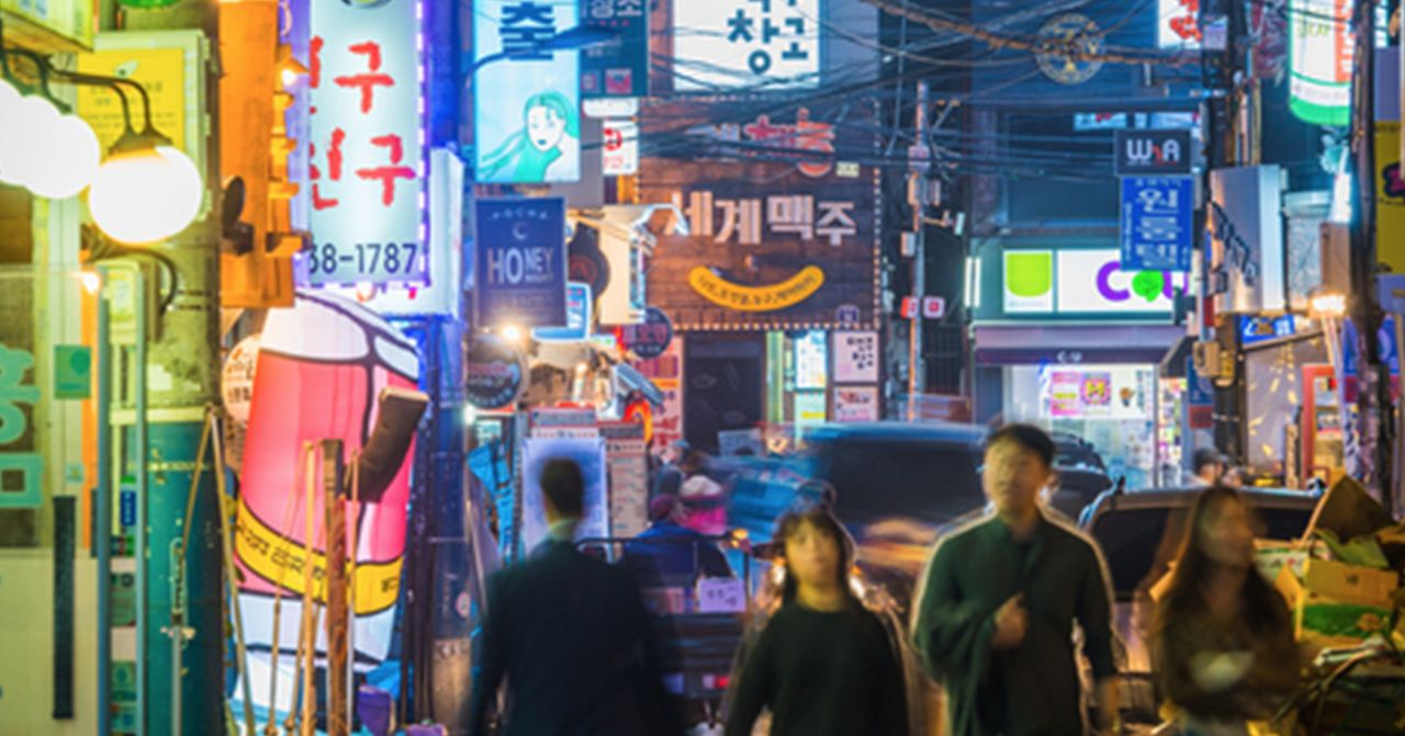 首爾繁忙的夜市街景，霓虹燈與光影瀰漫，眾人漫步其間，享受著多彩多姿的城市夜生活。
