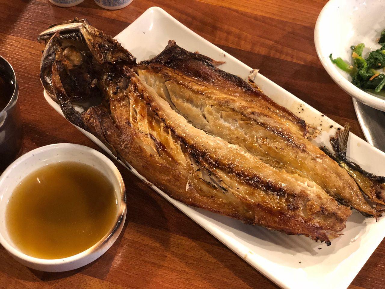 精緻擺盤的烤鯖魚，放在白色長盤中，魚皮金黃酥脆，搭配一碟淺棕色醬料，呈現典雅的韓國風味。