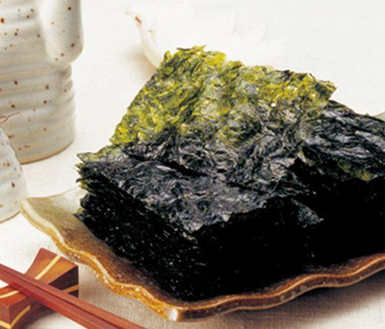 疊放成堆的韓國紫菜，襯於木製碟盤上，背後是米酒瓶，象徵著韓式餐桌的美味與健康。