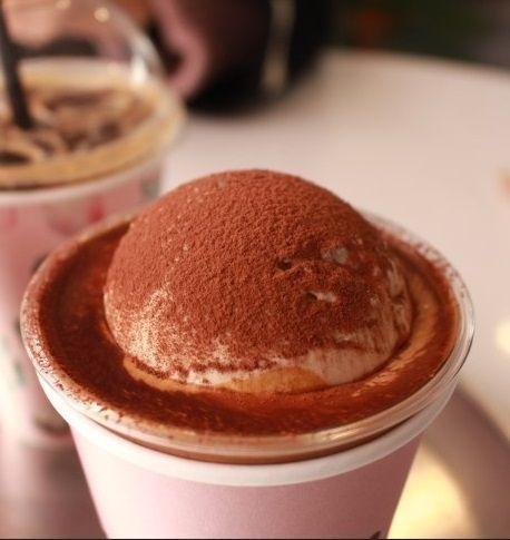 One In A Million咖啡廳的拿鐵，上面覆蓋有可可粉，放在簡約的粉色背景前。