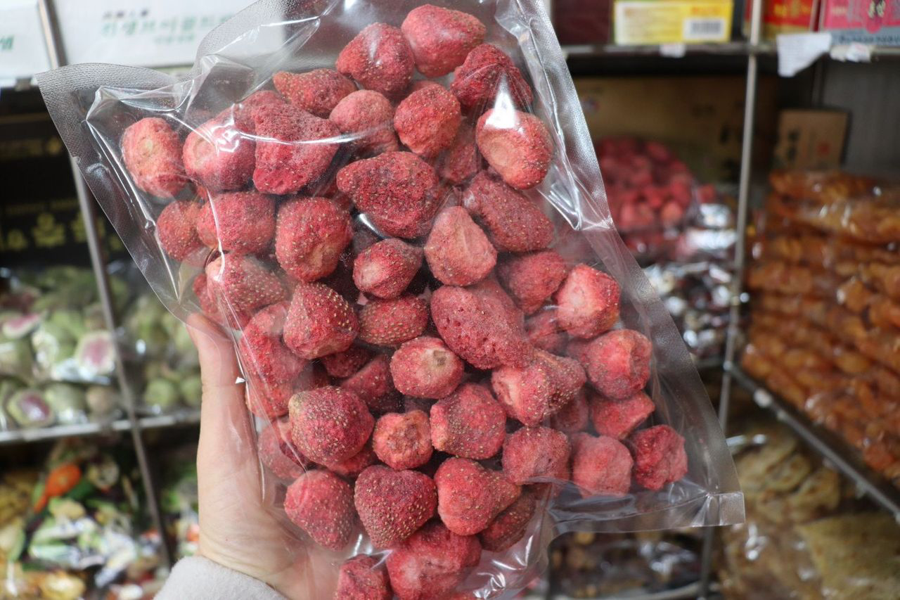 A hand showcasing a pack of dried strawberries, highlighting the vacuum packaging for freshness.