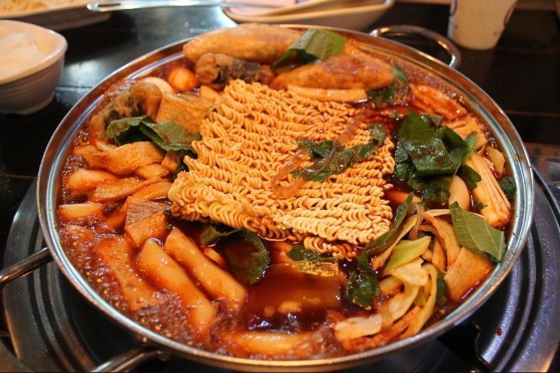 Colorful combination of Tteokbokki ingredients at Hwa Tteok, including noodles, quail eggs, and leafy greens in a rich, spicy broth.