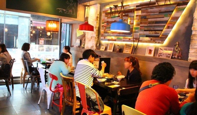 Interior of a cozy and vibrant restaurant in Seoul, showcasing colorful lighting and diners having a meal at Hwa Tteok.