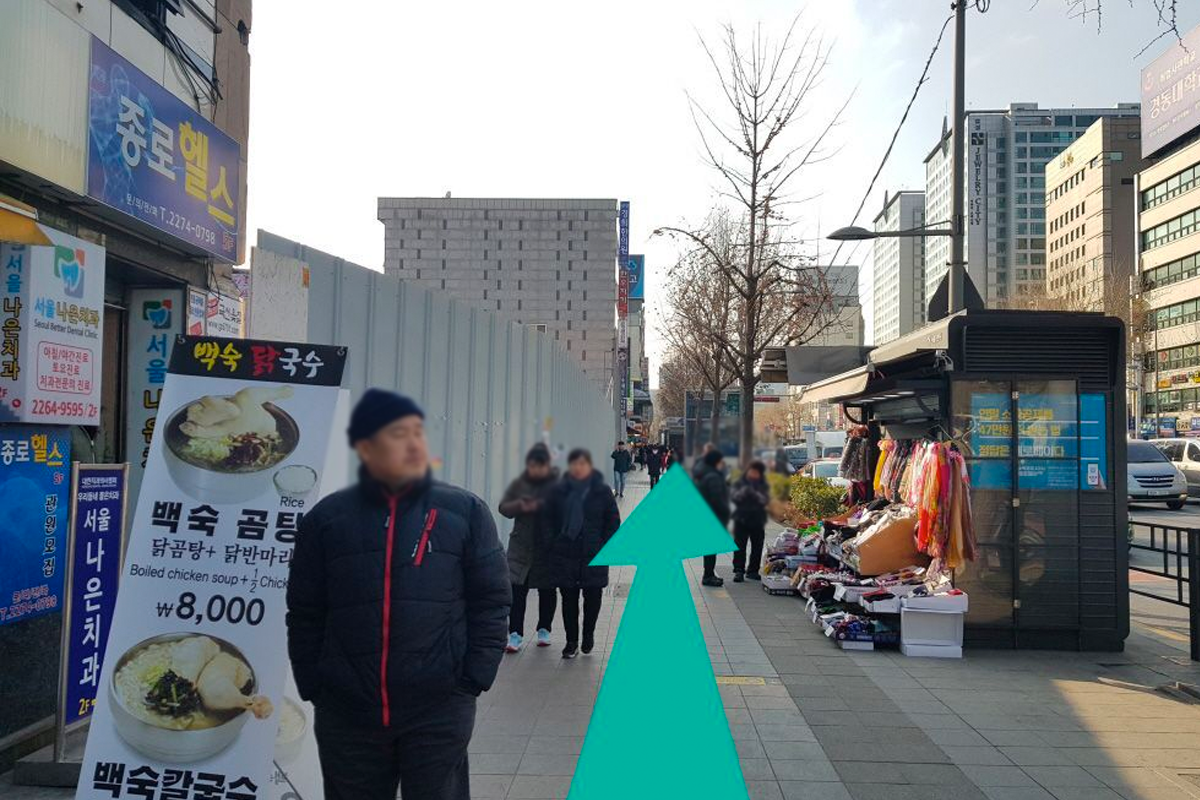 從鐘路5街出發，沿著箭頭方向前往廣藏市場的街景，這裡有許多商店與攤販，路邊擺放著各種商品。