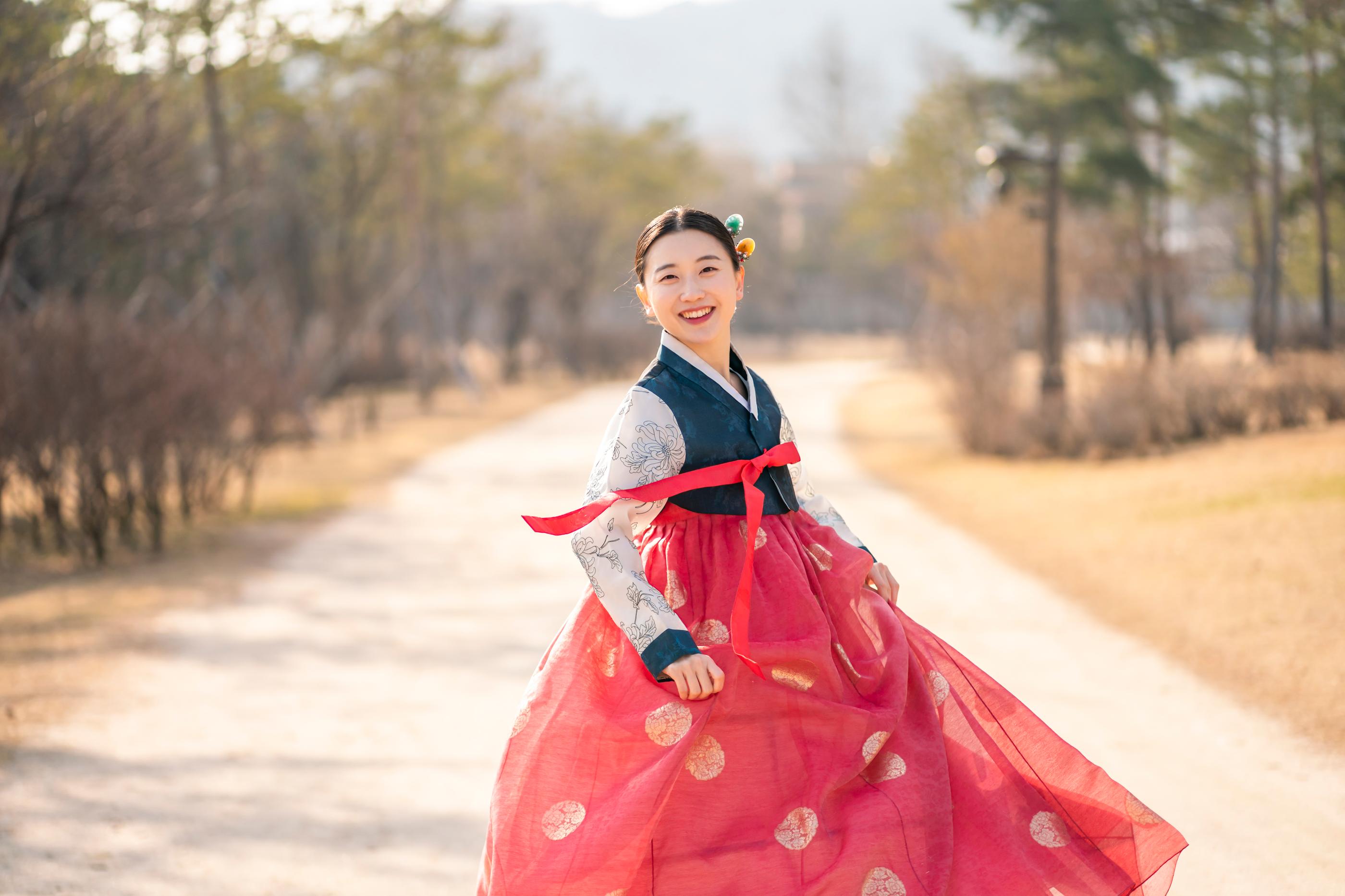 伝統的なスタイルの韓服、赤いスカートと白いジャケットを着用し、公園を歩く情景