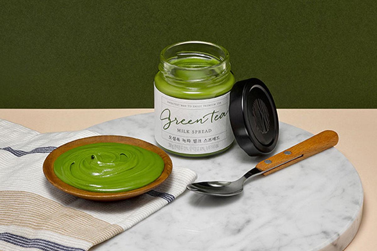 A jar of Osulloc Green Tea Spread on a tray next to a spoon, napkin and plate.
