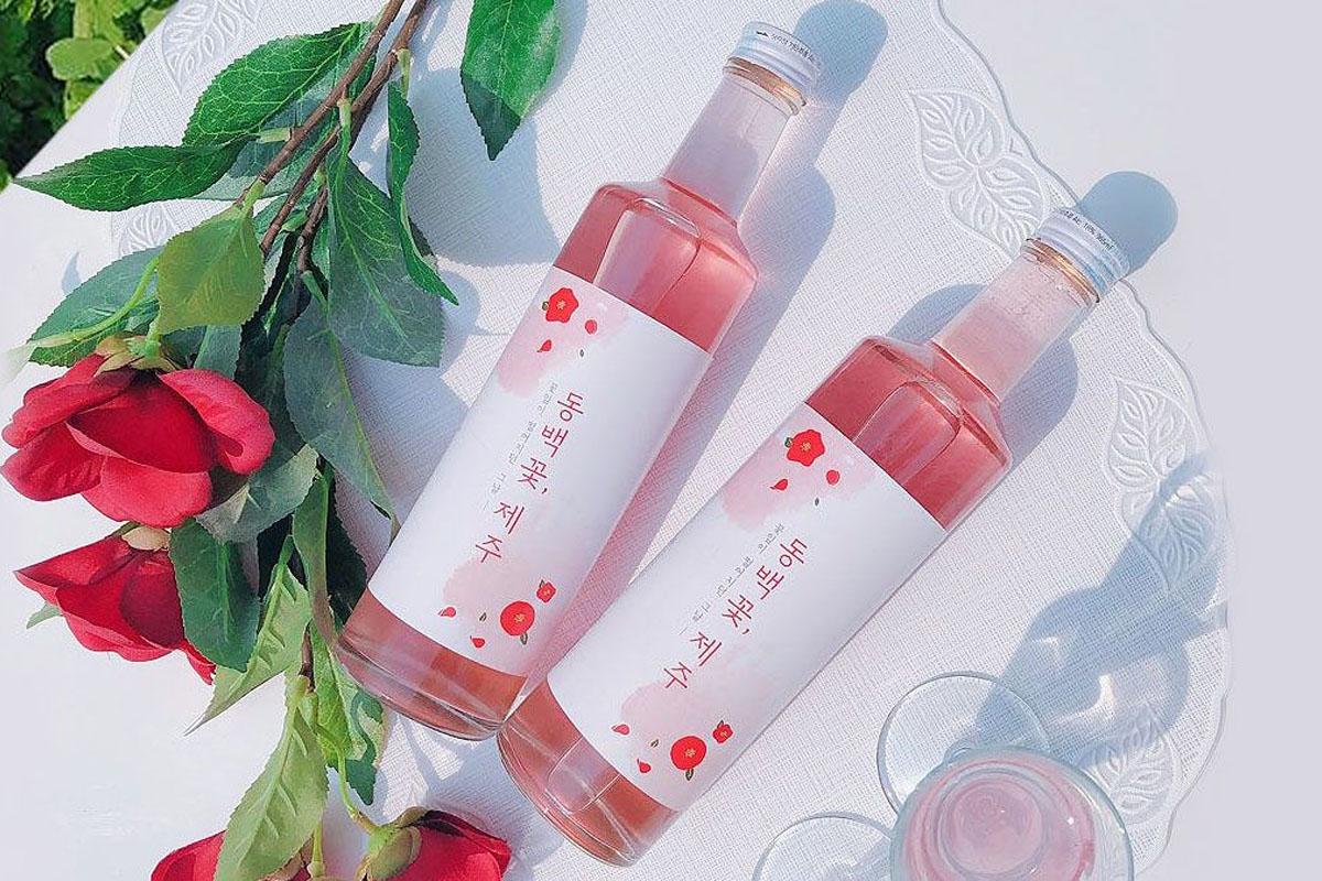 Two bottles of Camellia Jeju placed on a table with some roses.