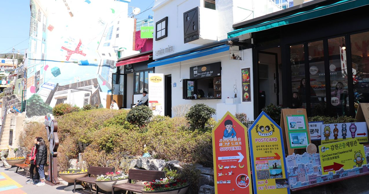 明信片架上擺放著各式甘川文化村主題的卡片，卡片色彩鮮豔，展示村莊的美麗景觀。