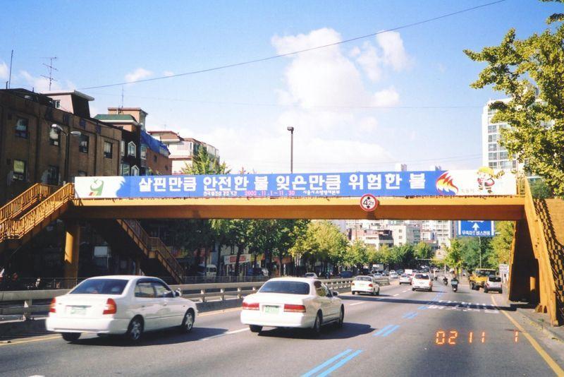 首爾街道上一座行人天橋，車輛沿著主要道路行駛，展示市區的日常交通流動。