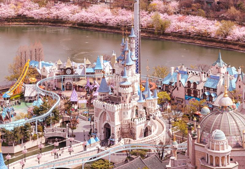 Arial view of Lotte World theme park in Seoul, displaying the amusement rides and a lake nearby.