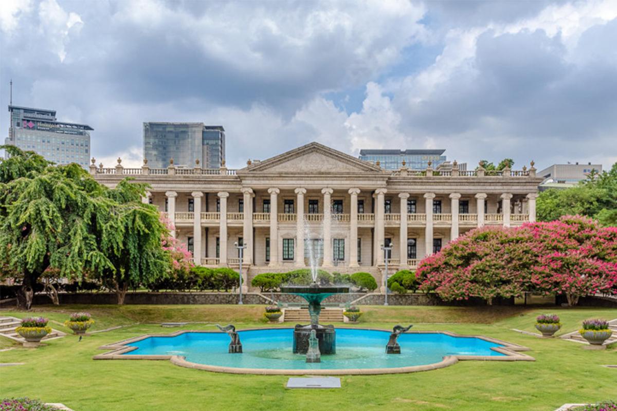 Exterior view of Deoksugung Palace in Seoul, highlighting its Western-style buildings and lush garden with a fountain.