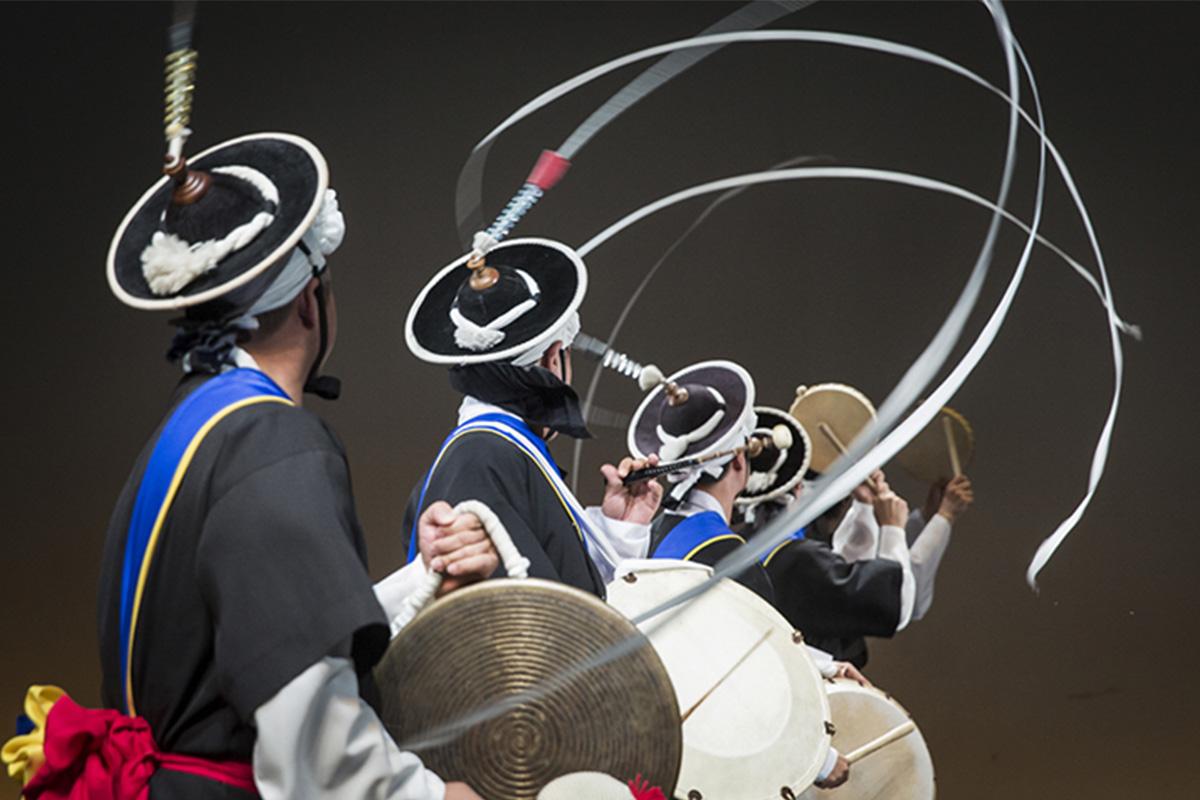 Traditionally dressed performers creating dynamic swirls with their ribbons and drums in a Korean folk performance.