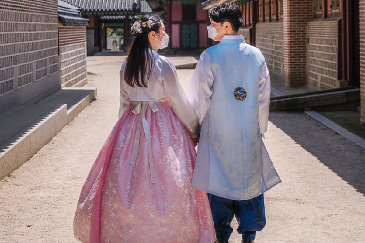 Couple dressed in hanboks walking along a historical site in Seoul, exploring Korean heritage.