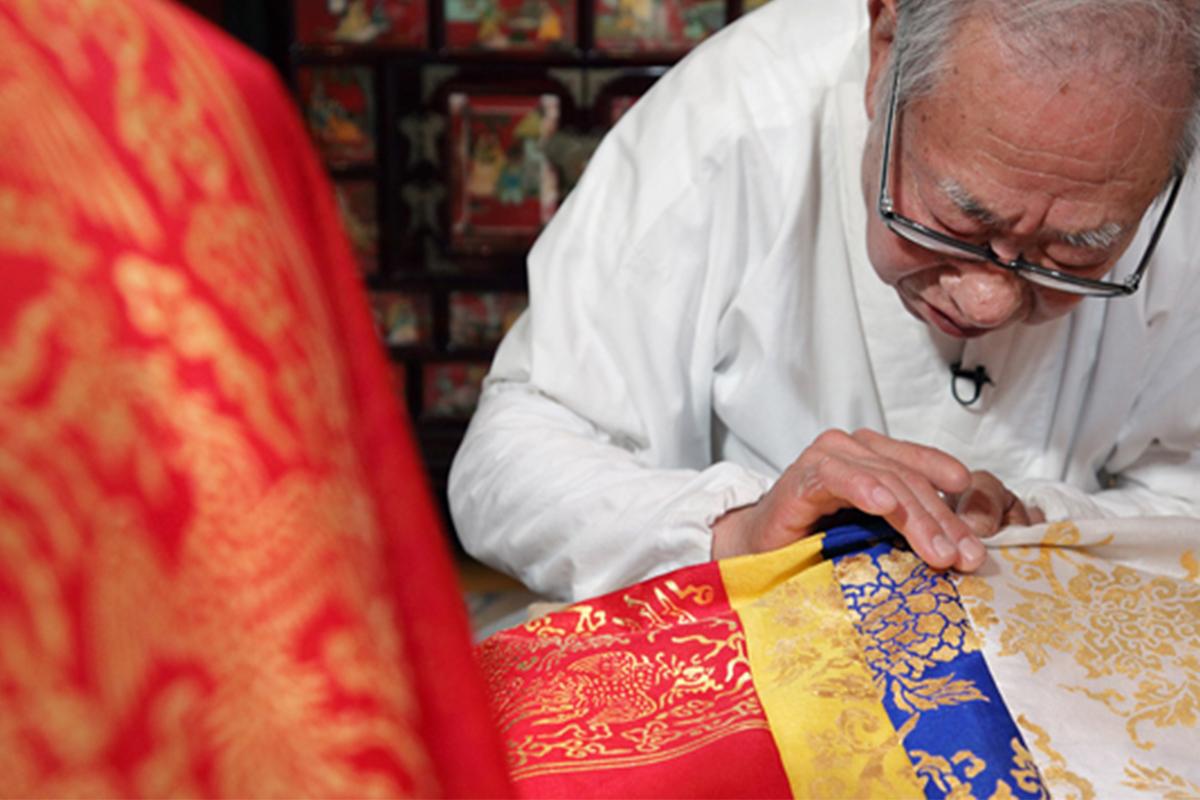 Artisan at work applying gold leaf details to traditional Korean fabric, demonstrating cultural heritage skills.