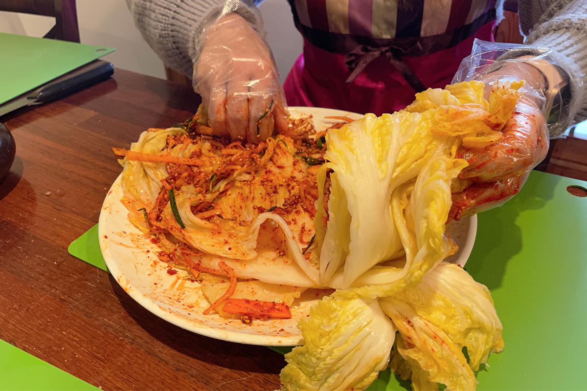 Inserting spices and vegetable mixture between cabbage leaves for kimchi processing.