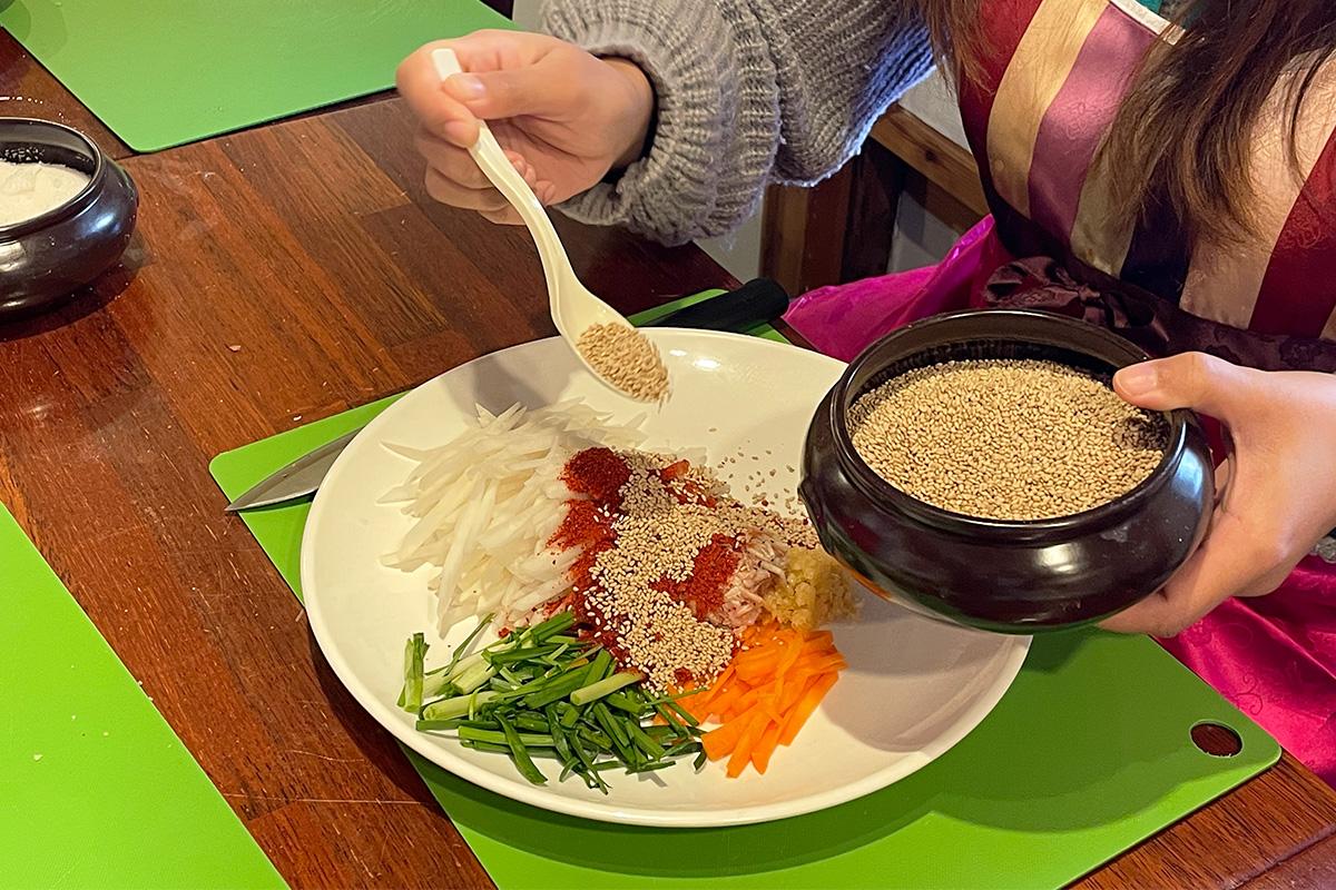 Adding sesame seeds to vegetables as part of the seasoning for kimchi preparation.