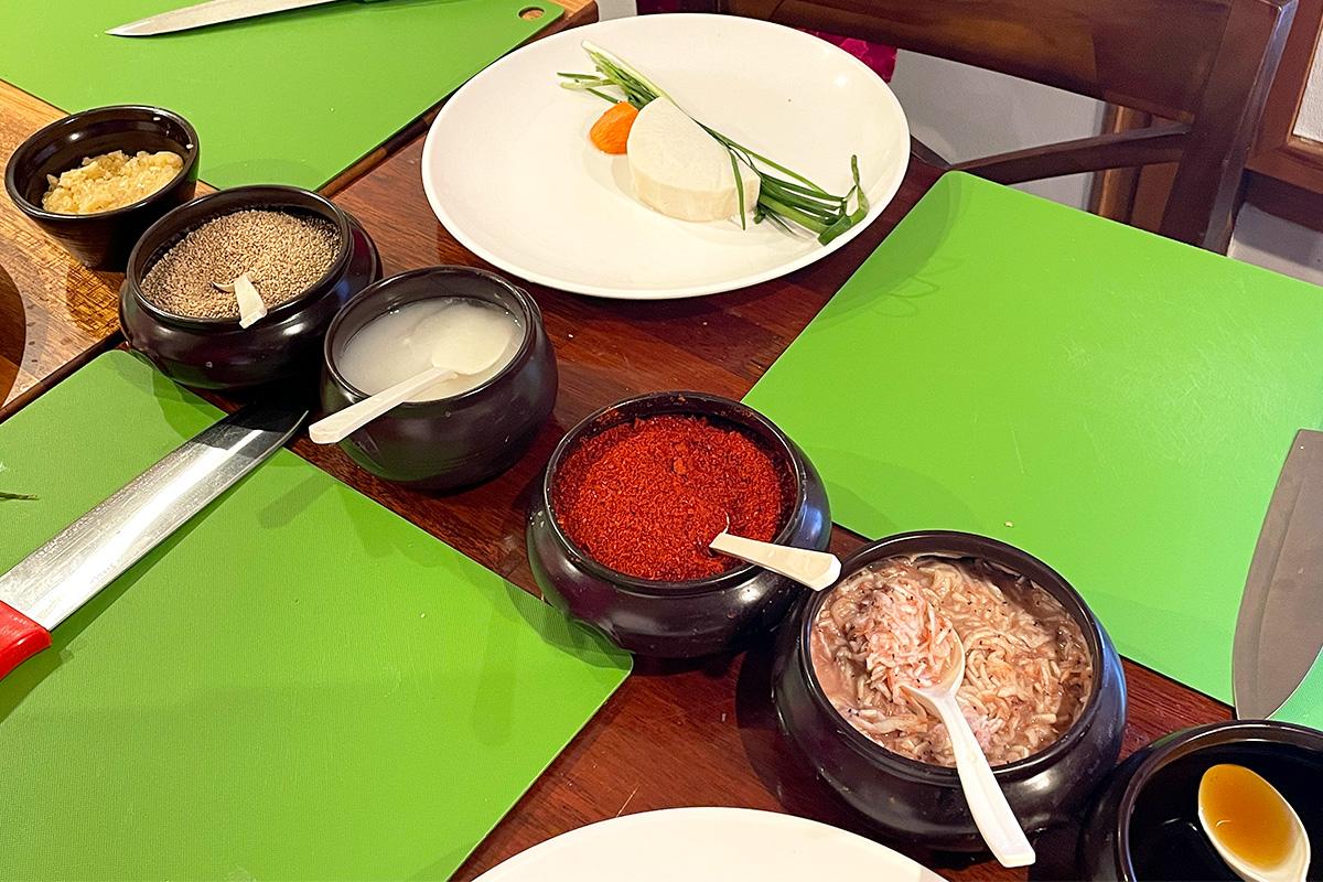 Various ingredients such as sesame, chili powder, and shrimp paste displayed for kimchi making.