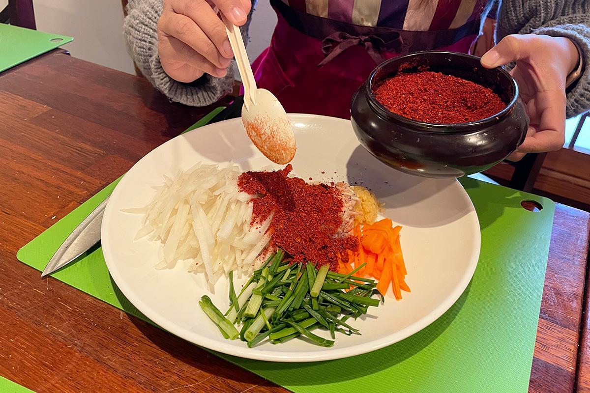 Adding chili powder to the vegetable mixture for creating homemade kimchi.