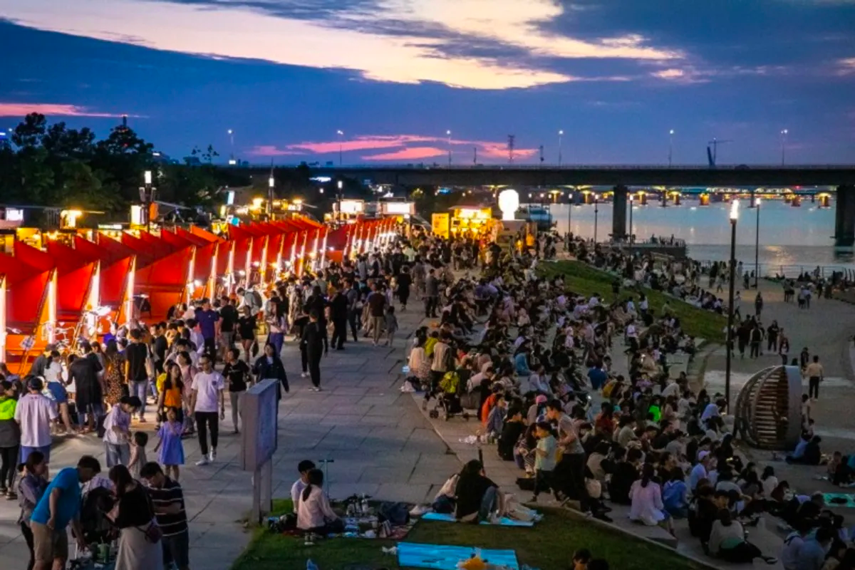 Dòng người tấp nập tại Chợ đêm trăng sông Hàn bên bờ sông với những gian hàng thức ăn và đồ uống sôi động dưới ánh hoàng hôn.