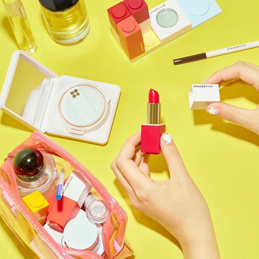石頭磚紅色唇膏及多樣彩妝用品，放於彩色化妝包及背景中。