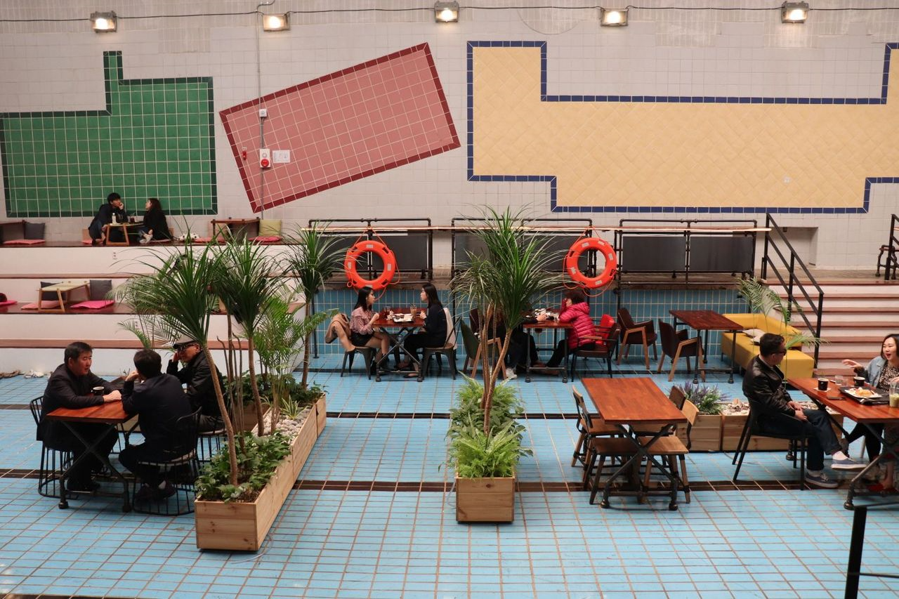 カフェジェムストーンの内部の様子。プールの底にテーブルや椅子が配置され、訪れた人々が楽しんでいる光景が見られます。白とブルーのタイルが特徴的なインテリアです。