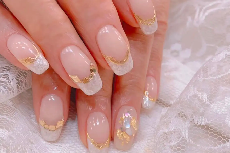溫和的白色指甲襯託著金色裝飾的精美美甲設計，展示典雅的樣式和細緻的襯底。