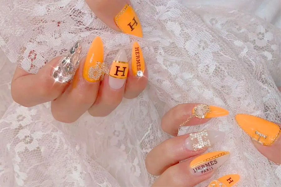 以橙色系為主的美甲設計，搭配Hermès字樣裝飾，展示於雙手上。